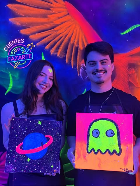 Dupla sorrindo e exibindo pinturas de planeta e personagem neon